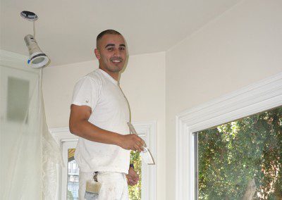 A man smiling and painting the house white wearing white