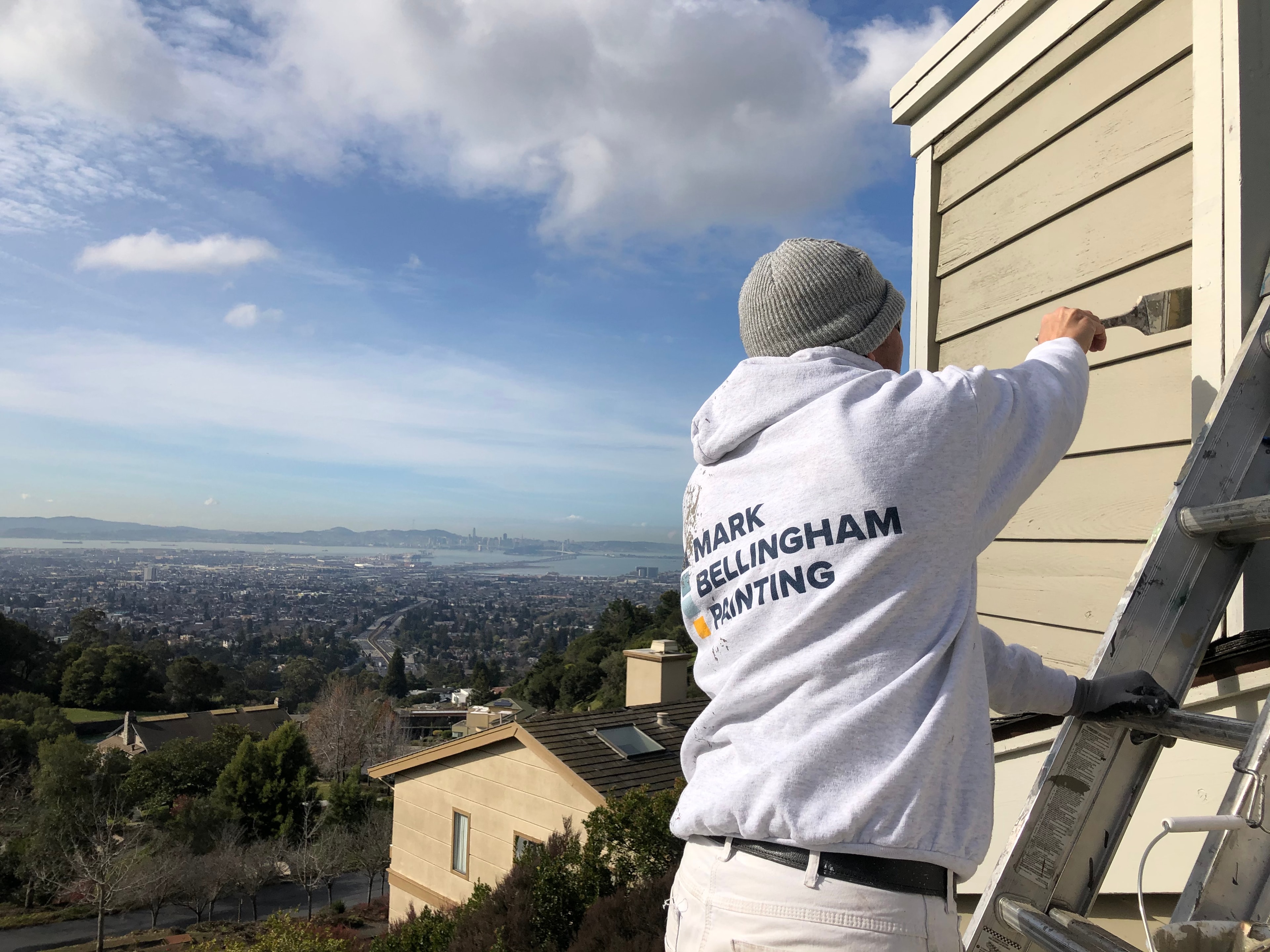 Mark Bellingham Painting craftsman on a ladder with the San Francisco Bay in the background
